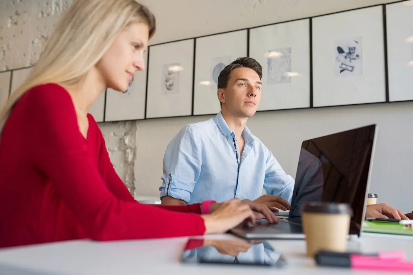 Un hombre y una mujer jóvenes y modernos trabajando en un portátil en una sala de oficina de coworking de espacio abierto.